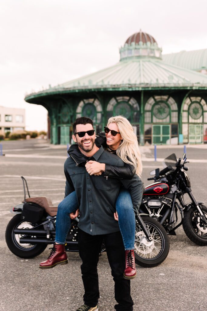  A couple celebrating their wedding anniversary with a custom motorcycle-themed photoshoot, embracing under a sunset backdrop in Asbury Park.